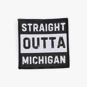 Op de afbeelding: Zwart-wit patch met de tekst "STRAIGHT OUTTA MICHIGAN". De tekst is in een distressed lettertype, met "OUTTA" in een witte rechthoek. De patch heeft een zwarte rand.