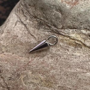 May include: A silver metal spike charm with a jump ring. The spike is pointed and has a smooth, shiny finish.