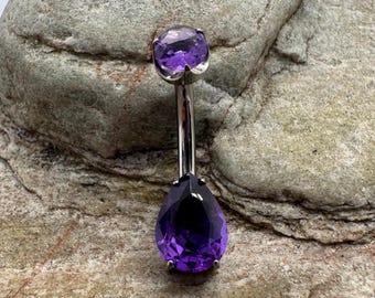 May include: A silver body piercing with a teardrop-shaped purple gemstone on the bottom and a round purple gemstone on the top.