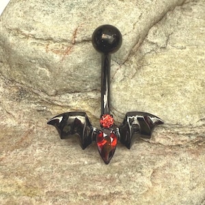 Può includere: Un piercing all'ombelico nero con un design ad ali di pipistrello. L'anello presenta una sfera nera nella parte superiore, una gemma rossa e un gruppo di gemme rosse. Le ali di pipistrello sono lucide e riflettono la luce.