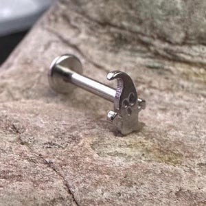 Op de afbeelding: Een zilveren body piercing met een klein gnoomontwerp. De gnoom draagt een hoed en heeft een baard.