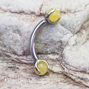 May include: A silver curved barbell with yellow gemstone ends. The barbell is made of surgical steel and is a popular choice for body piercings.