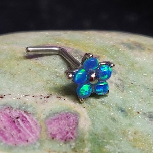 Könnte beinhalten: Ein silberner Nasenring mit einem blauen Opal-Blüten-Design. Die Blume hat sechs Blütenblätter und ist mit kleinen, runden Opalen besetzt.