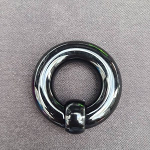 May include: A black circular ring with a smooth, shiny surface. The ring has a small, round knob on one side.