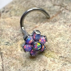 May include: A nose ring with a curved post and a flower-shaped design. The flower features multiple iridescent opal-like stones in shades of purple, blue, and green, set in a silver-colored metal.