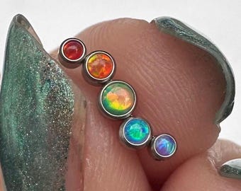 May include: A rainbow opal body jewellery piece with six small round gemstones in a rainbow colour gradient. The gemstones are set in a silver bar.