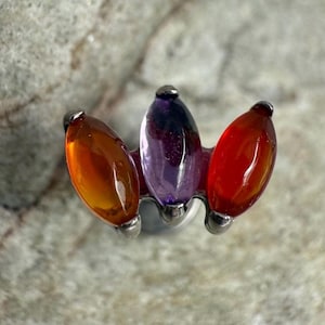 Puede incluir: Pendiente de botón plateado con tres gemas en forma de lágrima en naranja, morado y rojo. Las gemas están dispuestas en un grupo. El pendiente está diseñado para orejas perforadas.