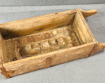 May include: A vintage wooden brick mold with a carved design. The mold is made of weathered wood and has a rectangular shape.