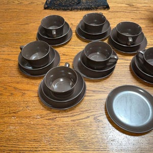 May include: A set of brown ceramic teacups and saucers. The cups and saucers are all the same color and have a simple, elegant design.