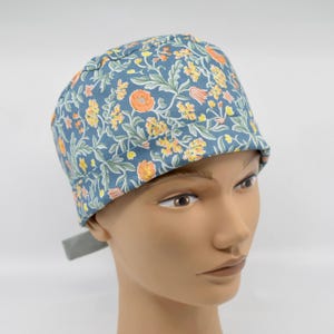 May include: A blue floral patterned scrub cap with orange and yellow flowers and green leaves. The cap is made of fabric and has a tie in the back. The cap is on a mannequin head.