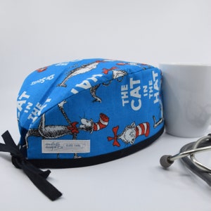 May include: Blue surgical scrub hat with a print of The Cat in the Hat characters. The hat has a navy blue trim and ties.