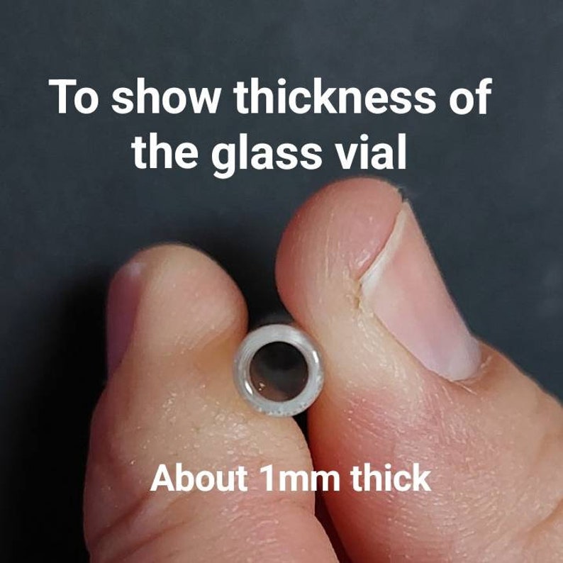May include: A close-up of a glass vial held between two fingers, showcasing its thickness. The text reads, "To show thickness of the glass vial" and "About 1mm thick."