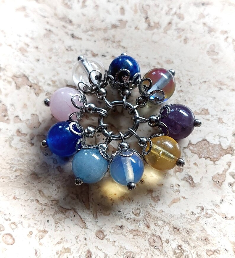 Puede incluir: Un brazalete con charms con una variedad de cuentas de piedras preciosas de colores, incluyendo transparentes, rosas, azules, moradas y amarillas. Las cuentas est&aacute;n unidas a una cadena de plata con detalles met&aacute;licos decorativos.
