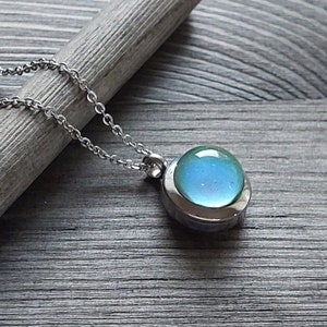May include: A silver chain necklace with a round pendant featuring a light blue glass orb encased in a silver setting.