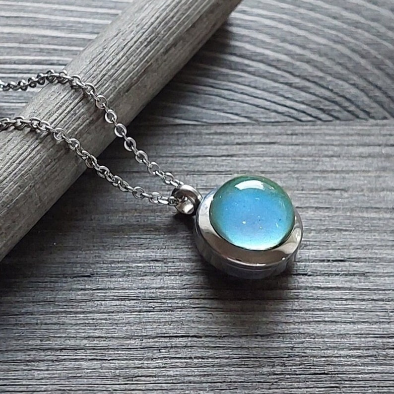 May include: A silver chain necklace with a round pendant featuring a light blue glass orb encased in a silver setting.
