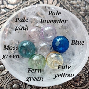 Pu&ograve; includere: Una collezione di sette piccole perline di vetro rotonde e traslucide in vari colori, tra cui rosa pallido, lavanda pallido, blu, verde muschio, trasparente, verde felce e giallo pallido, all'interno di una ciotola di vetro strutturato.