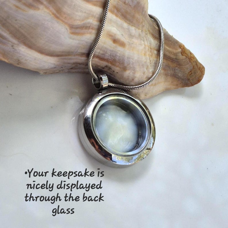 May include: A silver-toned circular locket pendant on a matching snake chain. The locket features a clear glass front and back, allowing for the display of small items inside. Text on the image reads: Your keepsake is nicely displayed through the back glass.