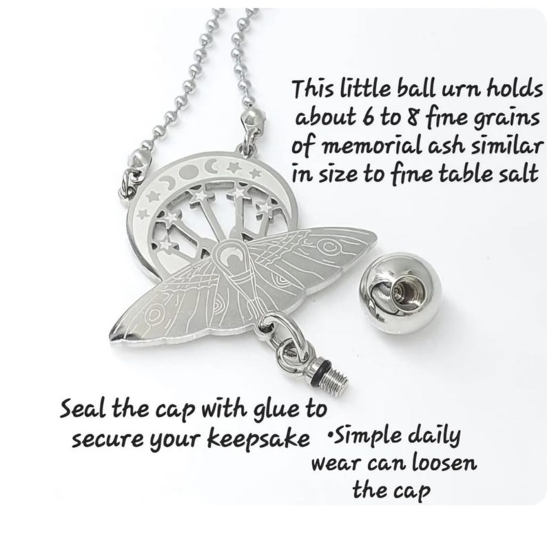 May include: A silver-toned metal pendant necklace featuring a moth and crescent moon design with stars. The pendant includes a small detachable ball urn with a threaded cap. Text states: This little ball urn holds about 6 to 8 fine grains of memorial ash similar in size to fine table salt. Seal the cap with glue to secure your keepsake. Simple daily wear can loosen the cap.