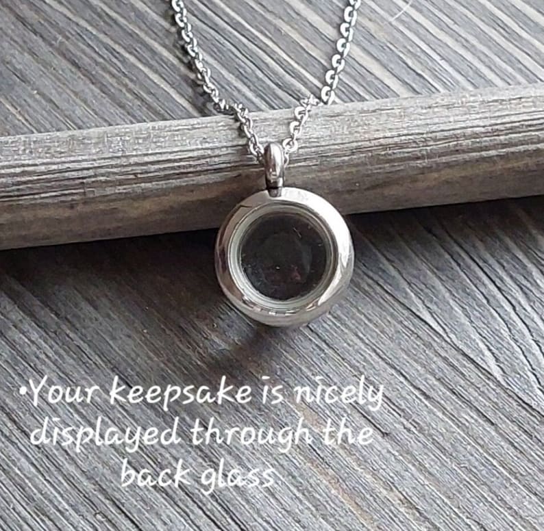 May include: A silver locket necklace with a clear glass insert. The locket is open and you can see the inside. The necklace is on a wooden surface.