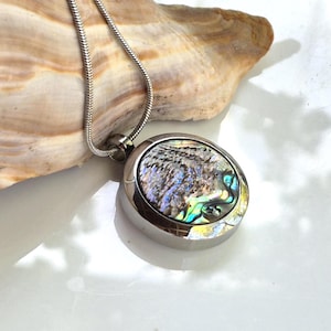 May include: A round silver-toned metal pendant necklace featuring an iridescent abalone shell inlay with swirling blue, green, and purple hues. The pendant hangs from a thin, flexible silver-toned snake chain, showcasing a polished metallic finish.