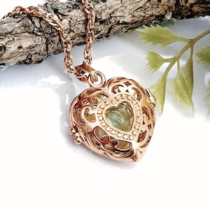 Pu&ograve; includere: Un ciondolo a forma di cuore color oro rosa con un intricato design in filigrana metallica. Il medaglione &egrave; appeso a una catena a corda ritorta abbinata e contiene una piccola pietra verde pallido visibile attraverso l'apertura centrale.
