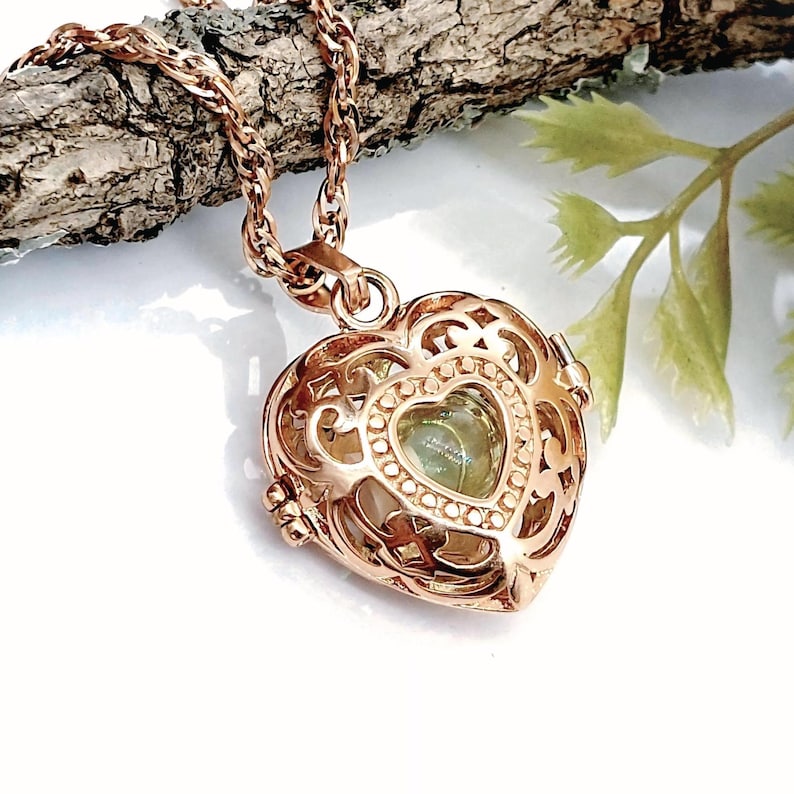 Pu&ograve; includere: Un ciondolo a forma di cuore color oro rosa con un intricato design in filigrana metallica. Il medaglione &egrave; appeso a una catena a corda ritorta abbinata e contiene una piccola pietra verde pallido visibile attraverso l'apertura centrale.