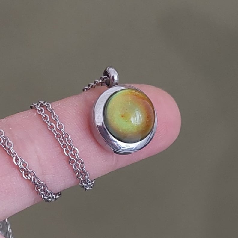 May include: A silver chain necklace with a round pendant featuring a green and yellow iridescent glass stone.
