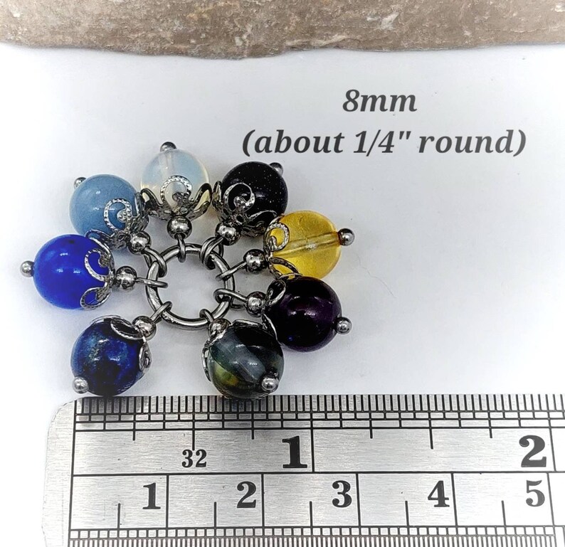 Puede incluir: Un brazalete con siete cuentas redondas de piedras preciosas de 8 mm de di&aacute;metro, en varios colores, incluyendo azul, morado, amarillo y negro. Las cuentas est&aacute;n unidas a una cadena de plata con detalles met&aacute;licos decorativos. El brazalete se mide con una regla, mostrando que las cuentas tienen un di&aacute;metro de aproximadamente 1/4 de pulgada. 8mm (aproximadamente 1/4" de di&aacute;metro)