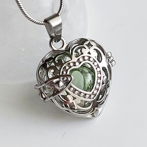May include: A silver heart-shaped locket necklace with an intricate design and a green glass charm inside.