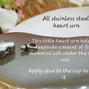 May include: A polished stainless steel heart-shaped urn with a detachable screw cap. The text reads: All stainless steel heart urn. This little heart urn holds a keepsake amount of fine memorial ash under the screw cap. Apply glue to the cap to seal it.