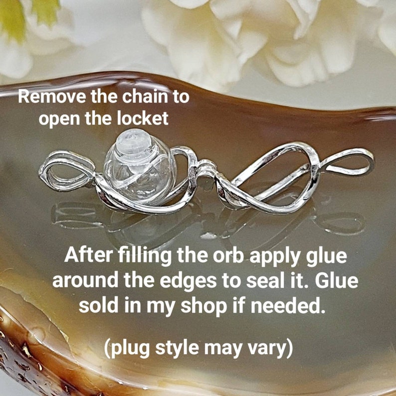 May include: A silver locket necklace with a clear glass orb pendant. The orb can be opened to hold a small amount of ashes or other mementos. The text "Remove the chain to open the locket" and "After filling the orb apply glue around the edges to seal it. Glue sold in my shop if needed. (plug style may vary)" is visible in the image.