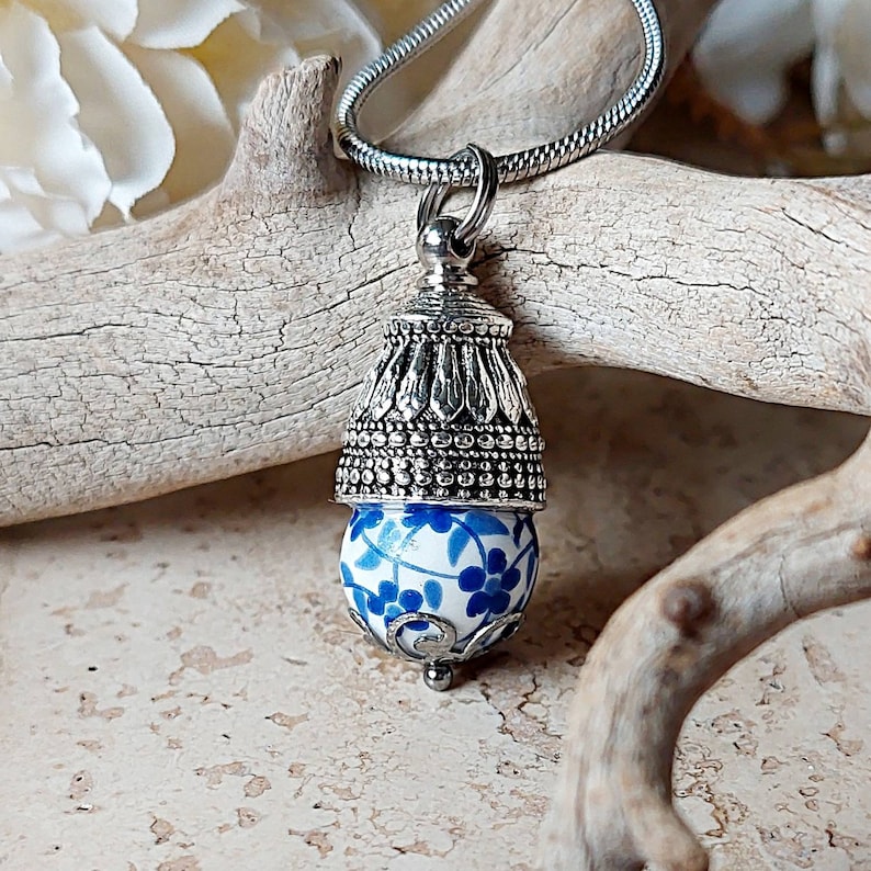 Puede incluir: Un collar de plata con un colgante de porcelana azul y blanco con un dise&ntilde;o floral. El colgante est&aacute; unido a una cadena de plata.