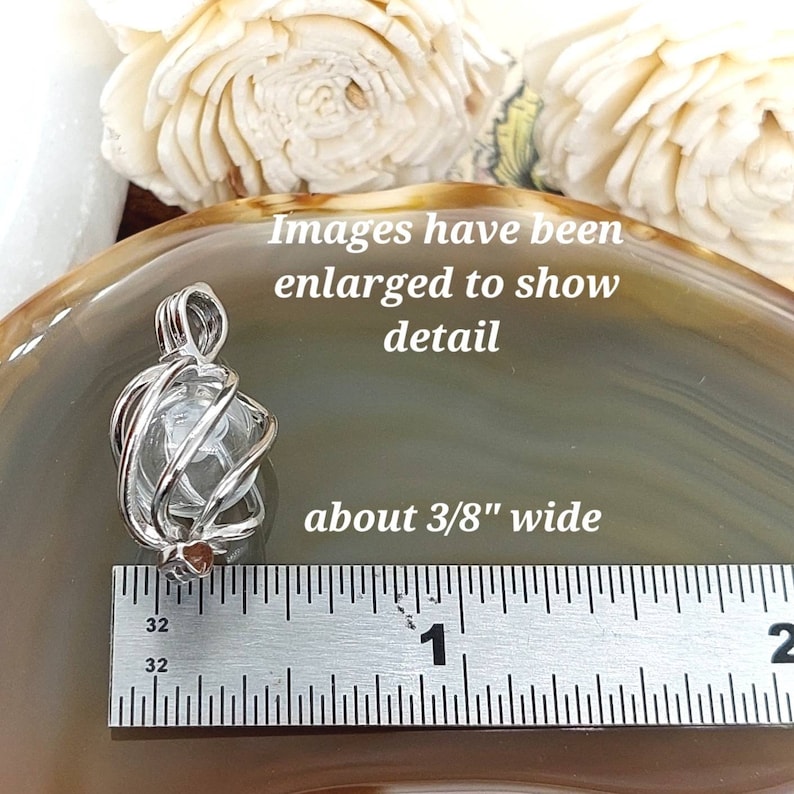 Puede incluir: Un colgante de cristal transparente, de aproximadamente 1 cm de ancho, encerrado en una jaula de alambre plateado. La imagen incluye el texto "Images have been enlarged to show detail" y "about 3/8" wide."
