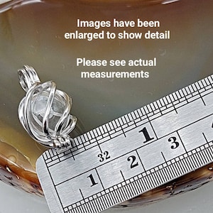 May include: A silver wire cage pendant with a clear crystal inside. The pendant is measured against a ruler, showing it is approximately 1 inch in diameter.