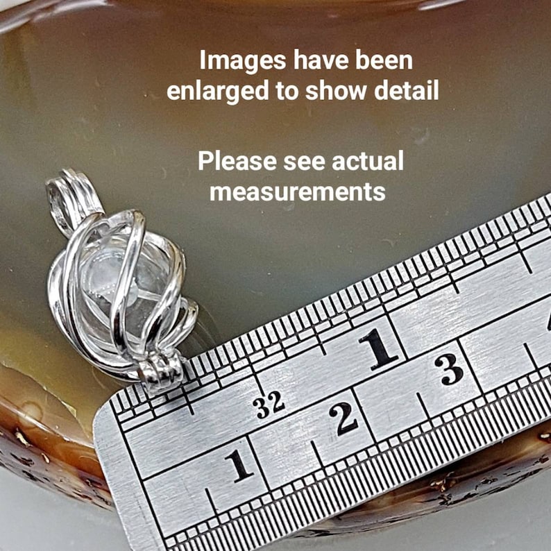 May include: A silver wire cage pendant with a clear crystal inside. The pendant is measured against a ruler, showing it is approximately 1 inch in diameter.