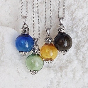 May include: Four glass orb pendants in blue, green, yellow, and dark brown, suspended from silver chains. Each orb has a decorative silver cap and base. The pendants are displayed against a white, textured background.