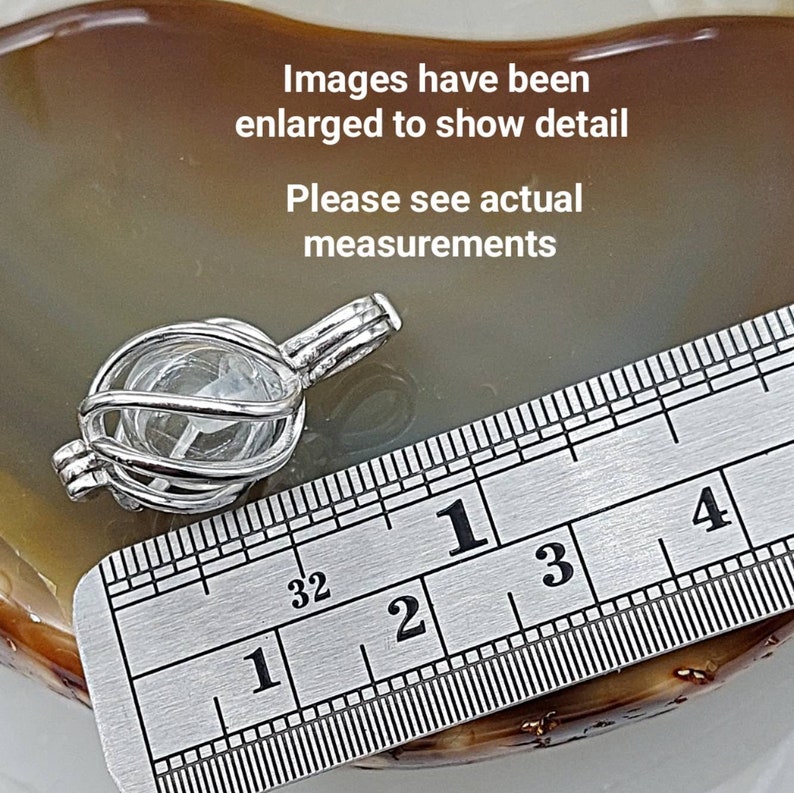 May include: A silver charm in the shape of a cage with a clear crystal inside. The charm is measured against a ruler, showing it is approximately 1 inch in diameter.