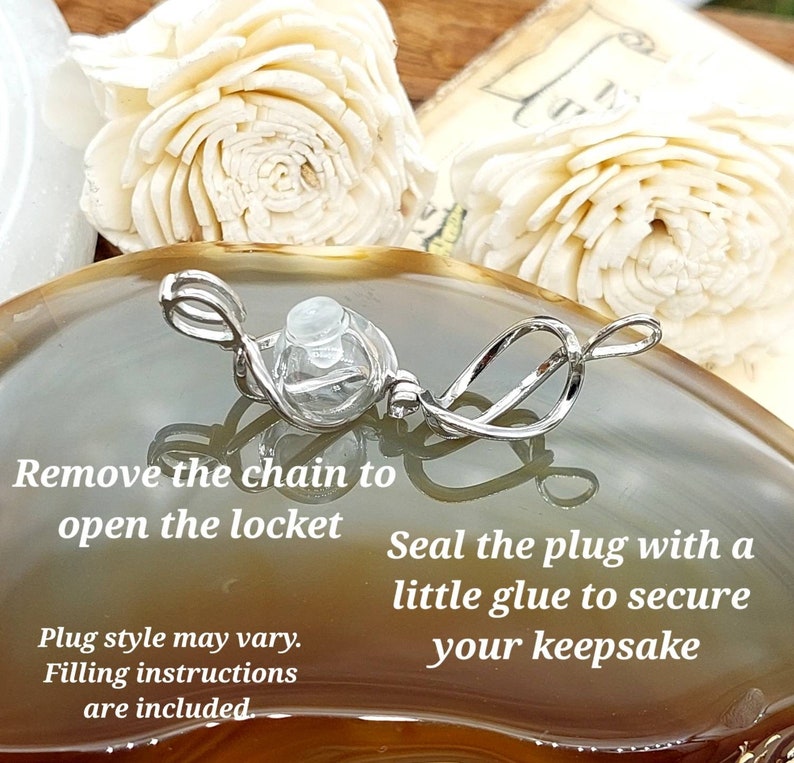 Puede incluir: Un relicario plateado con un globo de cristal transparente y un dise&ntilde;o decorativo en espiral. El texto de la imagen dice: "Retire la cadena para abrir el relicario. Selle el tap&oacute;n con un poco de pegamento para asegurar su recuerdo."