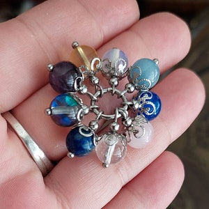 Puede incluir: Un brazalete de plata con un encanto con una variedad de cuentas de piedras preciosas de colores, incluyendo amatista, azul, verde, rosa y transparente.