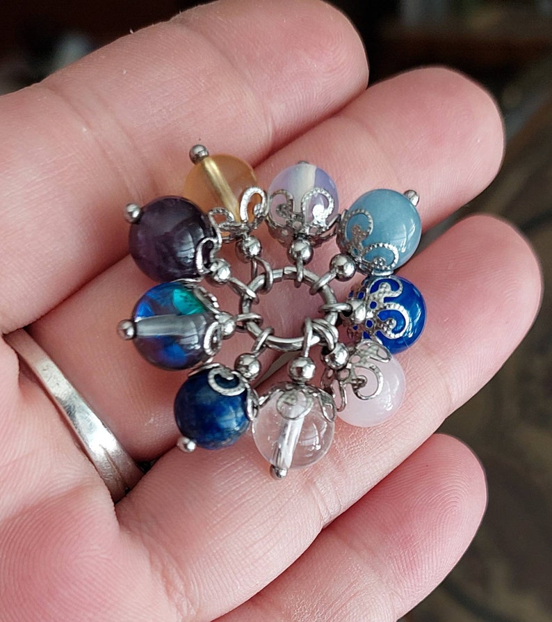 Puede incluir: Un brazalete de plata con un encanto con una variedad de cuentas de piedras preciosas de colores, incluyendo amatista, azul, verde, rosa y transparente.