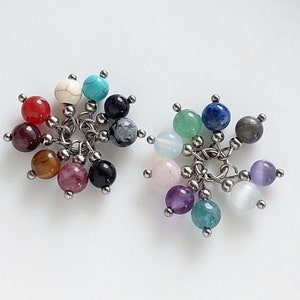 May include: A collection of 18 small, round, gemstone beads in various colors, including red, orange, yellow, green, blue, purple, and white. The beads are attached to silver metal rings, creating a decorative charm or pendant.