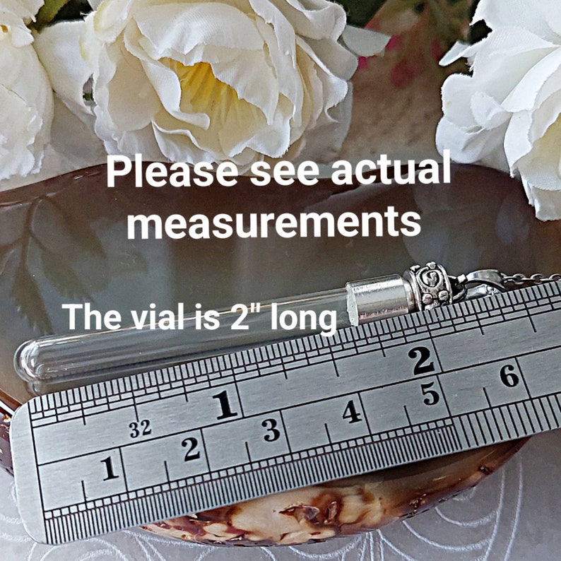 May include: A clear glass vial with a silver cap and a silver chain. The vial is 2 inches long and is measured against a ruler.