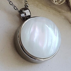Peut inclure: Un collier pendentif rond blanc avec un &eacute;clat nacr&eacute;. Le pendentif est serti dans un cadre en m&eacute;tal argent&eacute; et est suspendu &agrave; une cha&icirc;ne d&eacute;licate. Le collier est un bijou simple et &eacute;l&eacute;gant.