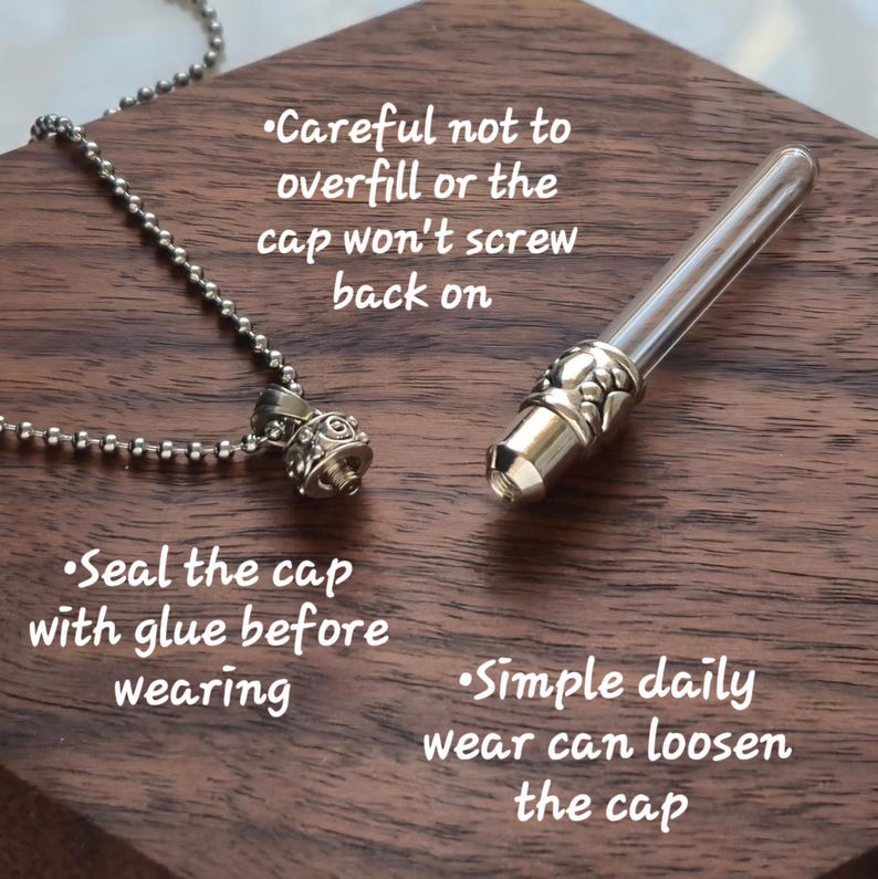 May include: A silver-colored necklace with a small, ornate pendant and a clear glass vial with a silver cap. The vial is detached, lying next to the pendant. Text on the wooden surface advises on use and care.