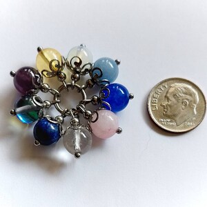 Puede incluir: Un brazalete con dijes con una variedad de piedras preciosas de colores, incluyendo amatista, azul, verde, rosa y amarillo. El brazalete est&aacute; hecho de plata y tiene un dise&ntilde;o delicado.