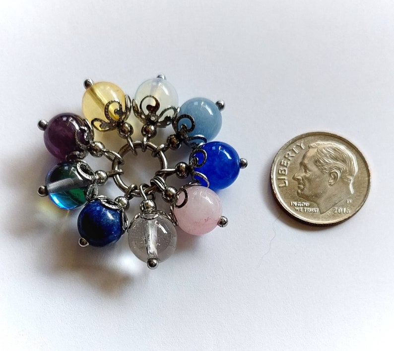 Puede incluir: Un brazalete con dijes con una variedad de piedras preciosas de colores, incluyendo amatista, azul, verde, rosa y amarillo. El brazalete est&aacute; hecho de plata y tiene un dise&ntilde;o delicado.