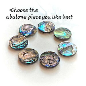 May include: Six circular abalone shell pieces arranged in a circle, each featuring iridescent blue, green, and brown patterns. The text "Choose the abalone piece you like best" is printed in dark gray above the shell pieces on a white background.