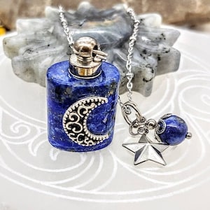 Puede incluir: Un collar de cadena de plata con un colgante de lapislázuli con forma de botella con un diseño de luna creciente. El colgante está unido a un amuleto de estrella de plata y una cuenta de lapislázuli.