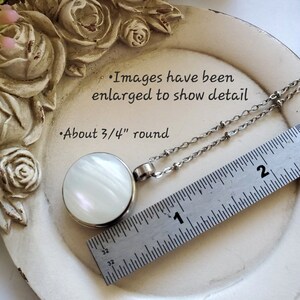 Peut inclure: Un collier pendentif rond avec un centre en nacre, d'environ 1,9 cm de diam&egrave;tre, serti dans un m&eacute;tal argent&eacute;. La cha&icirc;ne du collier est &eacute;galement argent&eacute;e. Le texte de l'image indique "Images have been enlarged to show detail" et "About 3/4" round."