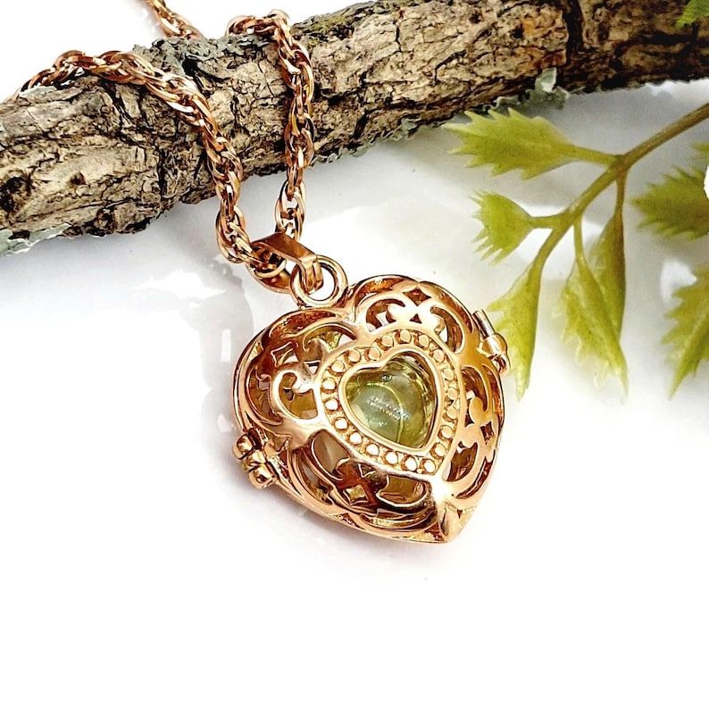 Pu&ograve; includere: Un ciondolo a forma di cuore color oro rosa con un intricato design in filigrana metallica. Il medaglione &egrave; appeso a una catenina intrecciata abbinata e contiene una pietra verde pallido a forma di cuore visibile attraverso le aperture.